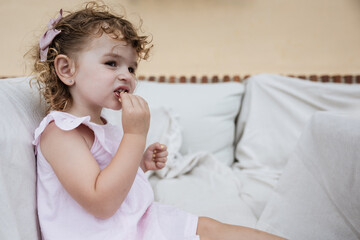 Two-year-old girl eating a snack while sitting on a sofa.