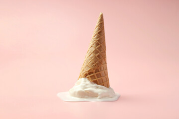 Melted ice cream in wafer cone on light pink background