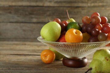 Glass vase with different fresh fruits on wooden table, closeup. Space for text