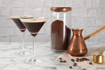 Refreshing cocktails in glasses, beans, cezve and ground coffee on white marble table