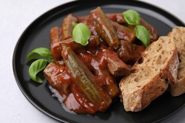 Tasty stew with okra, tomato sauce, bread and basil on white table, closeup