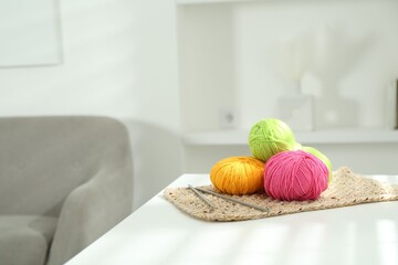 Skeins of soft yarn and knitting needles on white table indoors, space for text