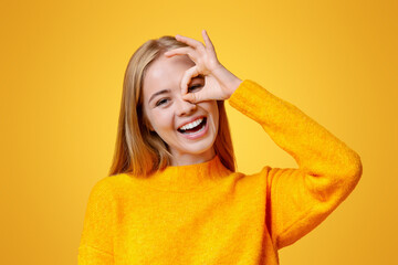 Everything is ok. Cheerful teen girl showing ok sign, gesturing with fingers near her eye, orange background