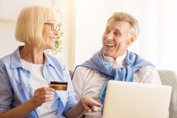 Modern mature couple shopping online on laptop, using credit card when choosing new clothes