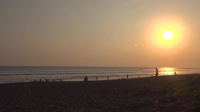 A wide of people sitting and playing on the beach at sunset in El Paredon, Guatemala