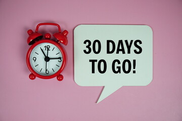 30 Days to go text on speech bluble with alarm clock top view on pink background