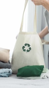 A woman puts old clothes in a textile bag with a recycling symbol. Reuse, recycling of materials and reducing waste in fashion, the idea of second hand clothes. Zero Waste Concept