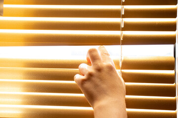 Little boy's hand opening yellow blinds on a window