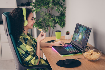 Photo of positive good mood girl dressed plaid shirt eating chips enjoying video games indoors...