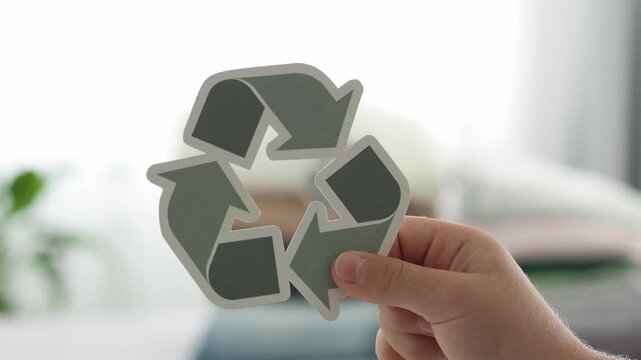 Close up of green RECYCLE symbol on blurred background, held by child's hand. Zero waste concept.