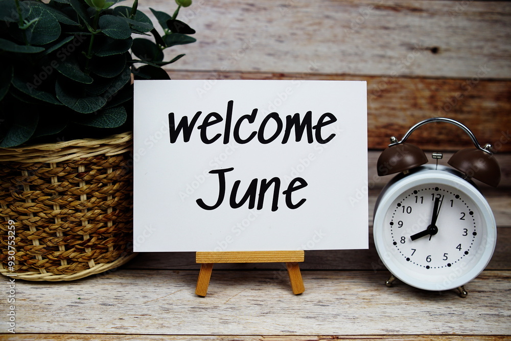 Poster welcome june text on paper card with alarm clock on wooden background
