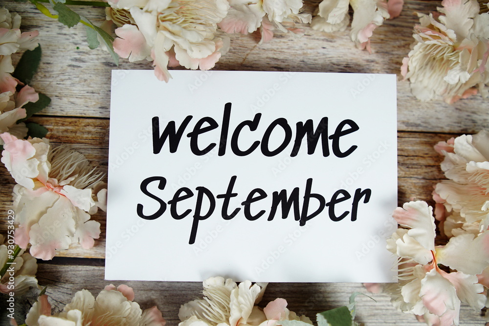 Wall mural Welcome September text on paper card with flowers frame top view on wooden background