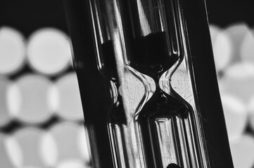 A black-and-white hourglass close-up measuring time with flowing sand transparent glass