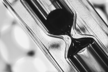 A black-and-white hourglass close-up measuring time with flowing sand transparent glass
