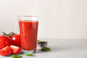 Tasty tomato juice in glass, basil leaves, peppercorns and fresh vegetables on light grey table, space for text
