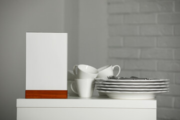 Menu holder and clean dishware on white table indoors