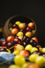 Cherries of different colours poured on the table from a clay pot, dark background, close-up