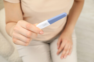 Woman holding pregnancy test indoors, closeup view