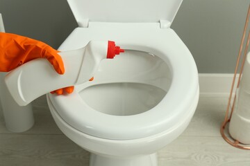 Woman cleaning toilet with detergent in bathroom, closeup
