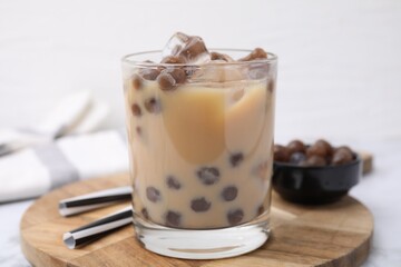 Tasty milk bubble tea in glass, tapioca pearls and straws on table, closeup