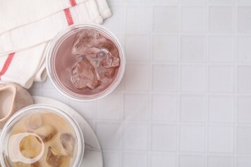 Tasty bubble tea in plastic cups on white tiled table, top view. Space for text