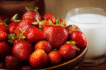 Red ripe strawberries in a brown clay plate with a glass of milk on the background