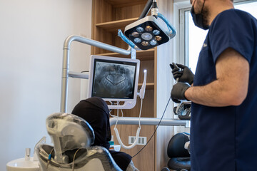 Conversation between dentist and muslim female wearing hijab looking at her tooths x-ray scan on...