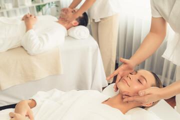 Fototapeta premium Caucasian couple enjoying relaxing anti-stress head massage and pampering facial beauty skin recreation leisure in dayspa modern light ambient at luxury resort or hotel spa salon. Quiescent