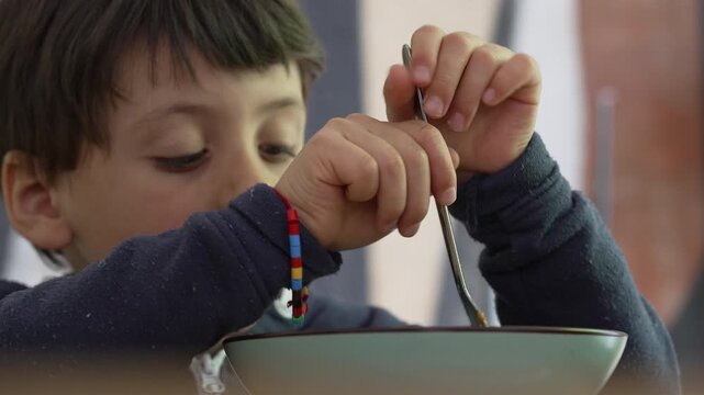 Child twirling spaghetti with a fork, concentrating deeply on the task, emphasizing the process of self-feeding and the focused effort in a familiar home setting