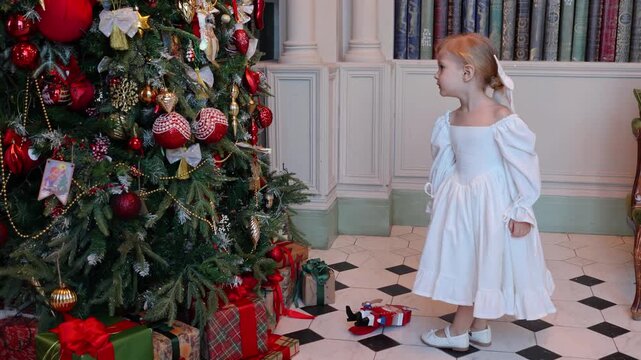 A cute little girl in a white dress and a Nutcracker, a New Year's tale about a revived toy, a Christmas mood, a Christmas tree dressed up for the holiday