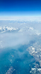 Out of this World Views Flying Over Greenland. Snow-capped mountains, glaciers and pristine terrain. Clear blue skies above the horizon.