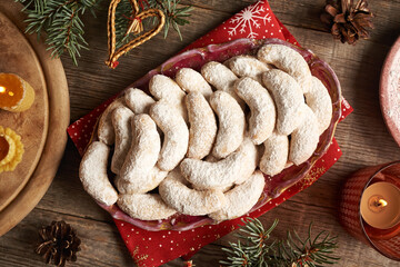 Top view of homemade Christmas cookies called Kipferl or vanilla crescents on a plate with candles and spruce tree branches