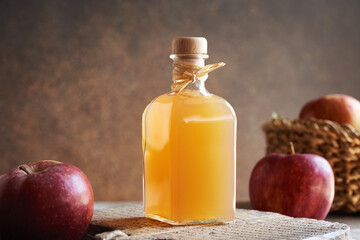 A transparent glass bottle of apple cider vinegar with fresh apples