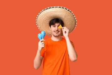 Portrait of young man with sombrero, maracas and tortilla chip on orange background. National...