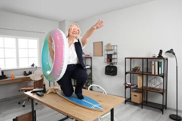 Mature businesswoman with swim ring and surfboard on table ready for summer vacation in office