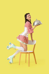 Young pin-up waitress on roller skates with tray and chair on yellow background