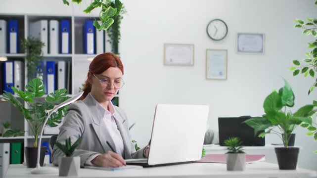 woman in glasses working on laptop against background of female slacker in office