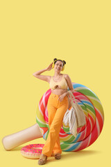 Smiling young woman in headphones with bag and inflatable mattress on yellow background