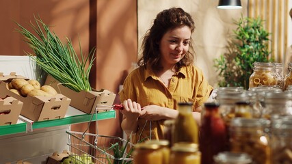 Vegan woman in specialty zero waste supermarket tasting pantry items before adding them to shopping...