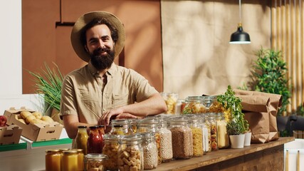 Portrait of smiling vegan man in eco friendly zero waste supermarket using shopping basket to purchase bulk items in ecological containers. Client in local bio grocery shop buying additives free food