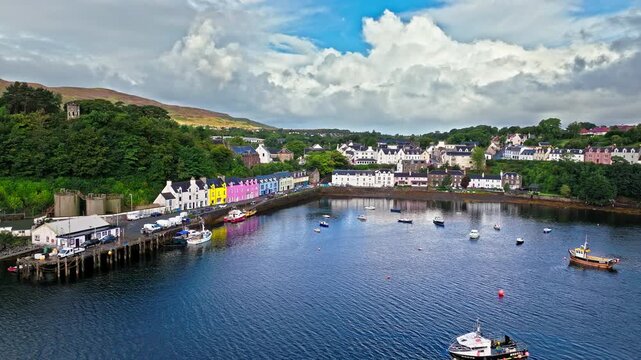 Aerial view of Portree town with colourful houses and fishing boats in Scotland. Scenic view of the natural harbour and port by high ground and cliffs. Popular tourist destination on the Isle of Skye.