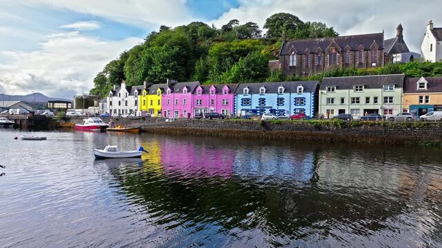 Aerial view of Portree town with colourful houses and fishing boats in Scotland. Scenic view of the natural harbour and port by high ground and cliffs. Popular tourist destination on the Isle of Skye.