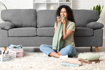 Beautiful young happy African-American woman folding clean clothes at home