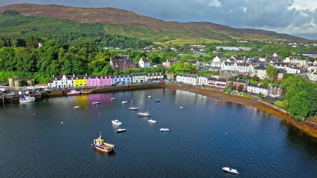 Aerial view of Portree town with colourful houses and fishing boats in Scotland. Scenic view of the natural harbour and port by high ground and cliffs. Popular tourist destination on the Isle of Skye.