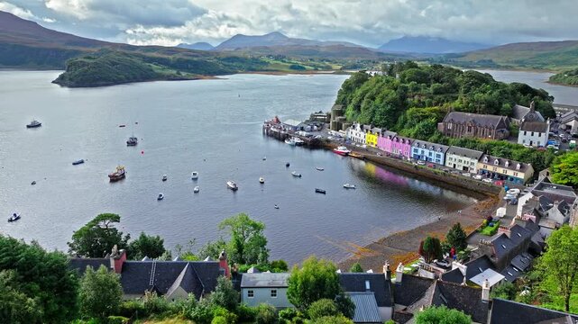 Aerial view of Portree town with colourful houses and fishing boats in Scotland. Scenic view of the natural harbour and port by high ground and cliffs. Popular tourist destination on the Isle of Skye.
