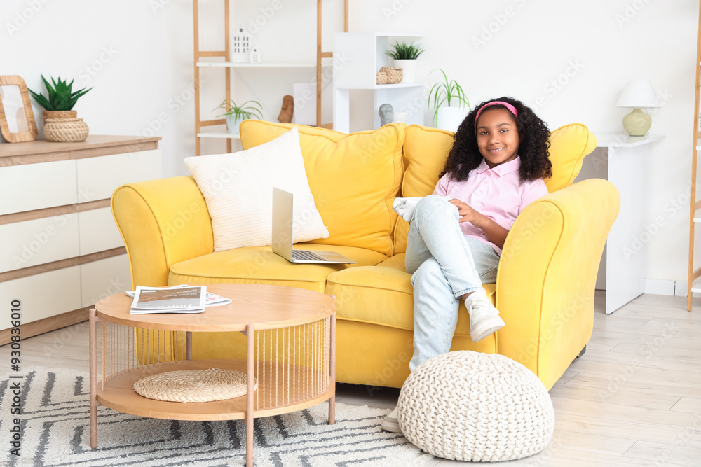 Poster little african-american girl with pencil case and laptop sitting on sofa at home