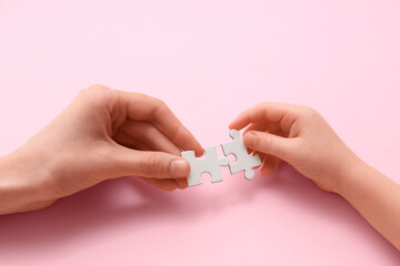 Female and child's hands with puzzle pieces on pink background, closeup