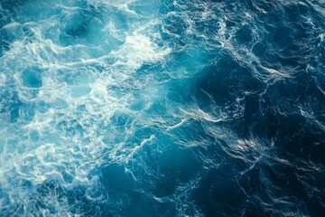 Top view of blue ocean water with intricate wave textures and water splashes, creating an abstract background of the sea surface, showcasing the dynamic movement and vibrant blue tones of the ocean.