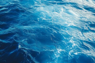 Top view of blue ocean water with intricate wave textures and water splashes, creating an abstract background of the sea surface, showcasing the dynamic movement and vibrant blue tones of the ocean.
