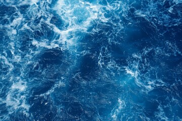 Obraz premium Top view of blue ocean water with intricate wave textures and water splashes, creating an abstract background of the sea surface, showcasing the dynamic movement and vibrant blue tones of the ocean.